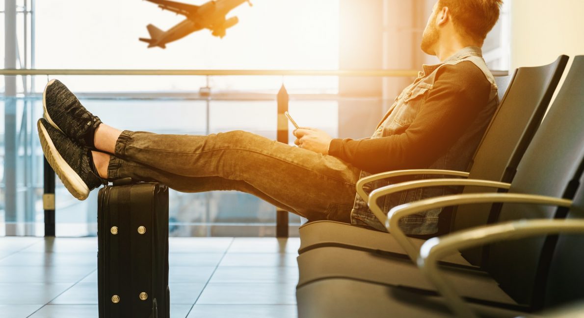 mand sidder i lufthavn og kigger på lettende fly